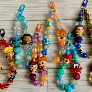 May include: A set of ten colorful beaded keychains with various Disney character charms. Each keychain features a different character, including Stitch, Moana, Ariel, and Rapunzel. The beads are made of glass and plastic and come in a variety of colors, including blue, pink, purple, and yellow.