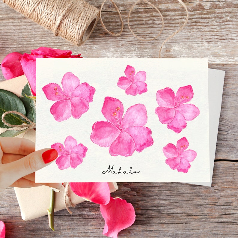 May include: A white card with the word "Mahalo" written in black cursive. The card is decorated with seven pink hibiscus flowers.