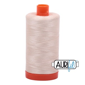Könnte beinhalten: Eine Spule Aurifil-Garn in hellbeige. Die Spule ist mit "Aurifil" in schwarzer Schrift auf weißem Hintergrund beschriftet.