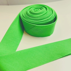 May include: A bright green fabric roll, unfurled to show the fabric's texture. The fabric is rolled up neatly, with the end of the roll lying flat.