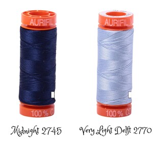 May include: Two spools of Aurifil thread, one in midnight blue and one in very light Delft blue. Both spools are labeled "Aurifil 100% Cotton" and have the color number printed below. The left spool is labeled "Midnight 2745" and the right spool is labeled "Very Light Delft 2770".