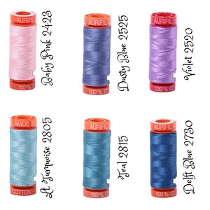 May include: Six spools of Aurifil thread in various colors, including baby pink, dusty blue, violet, light turquoise, teal, and delft blue. Each spool has a label with the color name and thread number.