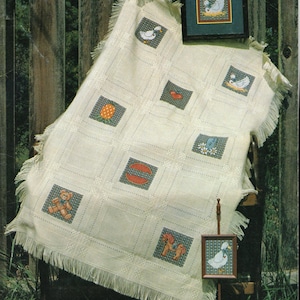 May include: A white crocheted blanket with a fringe border, featuring various cross-stitch designs of animals and objects. The blanket is displayed on a wooden chair with a small framed cross-stitch of a duck. The title "COUNTRY PATCHWORK" is printed at the top of the image, along with the text "by Judy M. Gibbs" and "Book 10".