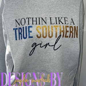 May include: Gray sweatshirt with the text "Nothin' Like A True Southern Girl" in black, blue, and gold glitter. The text "Designs By Jaylin Marleah" is in purple glitter.