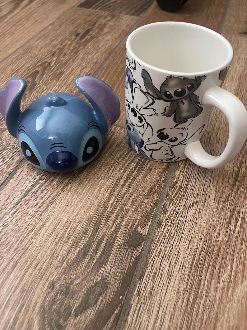 May include: A blue ceramic Stitch figurine and a white mug with Stitch character illustrations. The figurine has large ears and a detailed face. The mug features a white handle and a wrap-around design of the character.