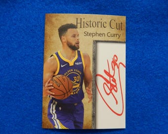 Könnte beinhalten: Eine Basketballkarte mit Stephen Curry von den Golden State Warriors. Die Karte hat einen goldenen Hintergrund mit dem Text "Historic Cut" und "Stephen Curry". Die Karte zeigt auch eine rote Unterschrift von Stephen Curry.
