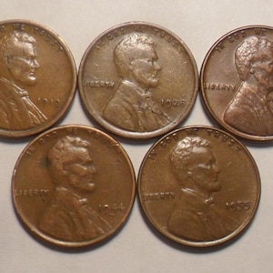 May include: Five vintage copper Lincoln pennies. Each coin features a profile of Abraham Lincoln and the word "Liberty." The years visible are 1919, 1928, 1940, 1944, and 1955. The coins are in various states of wear.