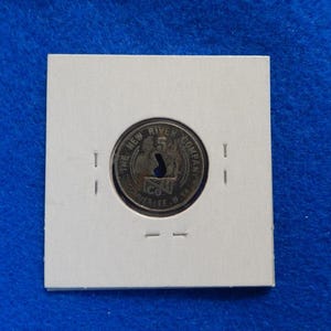 May include: A circular metal token from The New River Company, with text around the edge and a central keyhole design. The token is set in a white card with a blue background.
