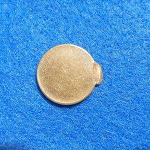 May include: A close-up of a copper-colored coin with a slightly bent edge. The coin is on a blue surface.