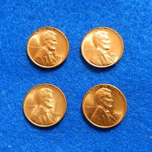 May include: Four copper-colored Lincoln pennies on a blue background. Each coin features a profile of a man and the words "IN GOD WE TRUST" and "LIBERTY". The years 1954, 1956, and 1957 are visible on the coins.