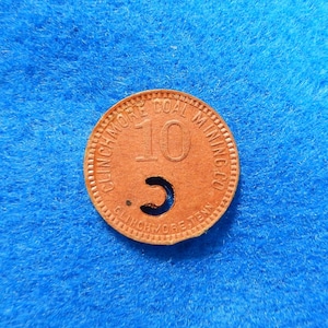May include: A copper-colored token with the text "Clinchmore Coal Mining Co." and the number "10" on it. The token has a hole in the center.