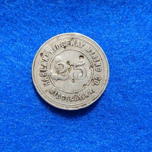 May include: A silver-colored round token with the text "HARLAN RIDGEWAY MINING CO." around the edge. The number "25" is in the center. The token is on a blue surface.