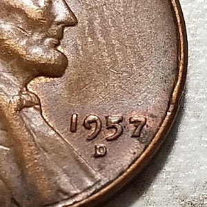May include: Close-up of a copper penny with the year 1957 and the letter D stamped on the side.