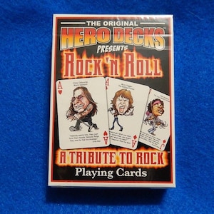 May include: A deck of "Hero Decks" playing cards titled "Rock 'N Roll: A Tribute to Rock." The box features the text "The Original" and images of playing cards with rock star caricatures. The background is blue.