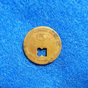 May include: A gold-colored metal token with the text "Fremont Wyoming Min. Co." and the number "5" in the center. The token has a cutout in the shape of a cross.
