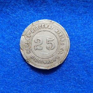 May include: A silver-colored token with the text "HARLAN-RIDGEWAY MINING CO. RIDGEWAY, KY." around the edge. The number "25" is in the center. The token is on a blue background.