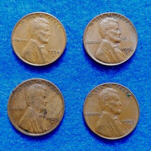 May include: Four copper-colored Lincoln pennies are displayed against a blue background. Each coin features a profile of a man and the inscriptions "IN GOD WE TRUST" and "LIBERTY", with the years 1954, 1956, 1929, and 1955 visible.