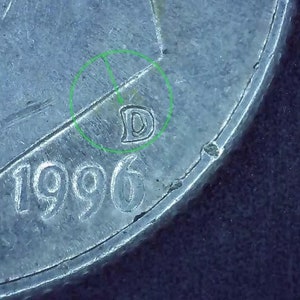 May include: Close-up of a silver coin with the year 1996 and the letter D stamped on it.