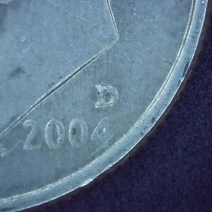 May include: Close-up of a silver coin with the year 2004 and the letter D stamped on it.