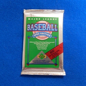 May include: A sealed 1990 edition Major League Baseball trading card pack. The pack has a green and white design with the words "BASEBALL" and "1990 EDITION" prominently displayed. A red banner reads "WIN!" on the right side.