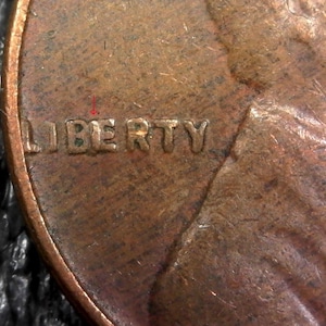 May include: Close-up of a copper penny with the word "LIBERTY" inscribed on the face.
