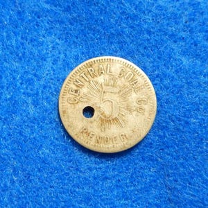 May include: A worn, circular metal token with the text "CENTRAL COAL CO." and "RENDER" around the edge. The number "5" is in the center, surrounded by a sunburst design. A small hole is near the center.