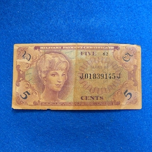 May include: A vintage five-cent note with a portrait of a woman. The note is tan with brown text and a serial number. The text on the note reads "FIVE" and "CENTS". The note is on a blue background.