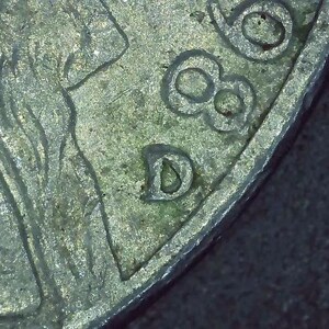 May include: Close-up of a silver coin with the letter "D" stamped on the side. The coin has a worn, aged appearance.