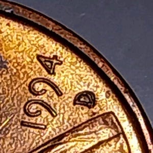 May include: Close-up of a copper-colored coin, featuring the year 1994. The coin's surface has a textured appearance, with the numbers and letters slightly raised. The coin's edge is visible, showing a slightly worn condition.