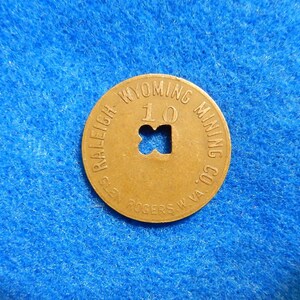 May include: A brass token with the text "WYOMING MINING CO.  RALEIGH ROGERS, W.VA." and "10" in the center. The token has a hole in the center.