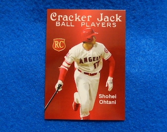 May include: A red, white, and blue Cracker Jack baseball card featuring Shohei Ohtani, a baseball player for the Los Angeles Angels. The card has the RC logo and the text "Cracker Jack Ball Players".