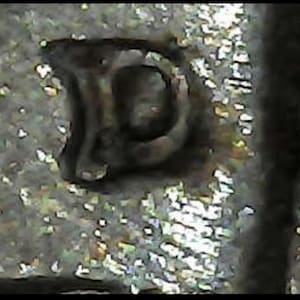 May include: Close-up of a silver metal object with the letter "D" stamped on it.