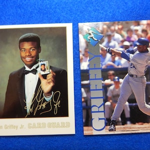 May include: Two baseball trading cards featuring Ken Griffey Jr. The card on the left shows Griffey in a tuxedo holding a baseball card of himself. The card on the right shows Griffey in a Seattle Mariners uniform swinging a bat. The text "CARD GUARD" is printed on the left card. The text "GRIFFEY" is printed on the right card.