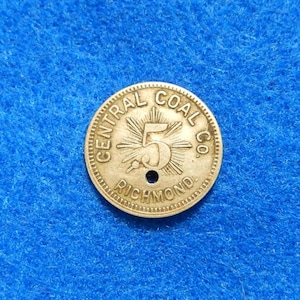 May include: A gold-colored coin with the text "CENTRAL COAL CO. RICHMOND" around the edge. The number "5" is in the center, surrounded by a sunburst design. A small hole is near the center.