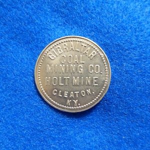 May include: A silver token with the text "Gibraltar Coal Mining Co. Holt Mine Cleaton, Ky." around the edge.