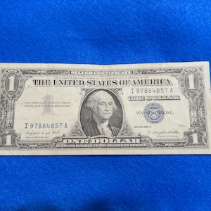 May include: A vintage one dollar silver certificate from the United States of America. The certificate features a portrait of George Washington and the text "This certifies that there is on deposit in the Treasury of the United States of America I 97884857 A One Dollar in silver payable to the bearer on demand."
