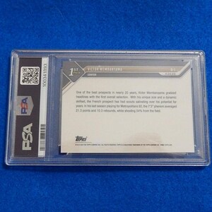 May include: A PSA-graded Victor Wembanyama Topps trading card encased in a clear plastic holder. The back of the card features white text on a light background, detailing the player's stats and history, with a QR code and PSA logo on the left side.