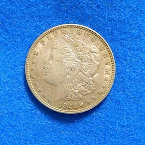 May include: A silver coin with a profile of a woman's face, surrounded by text and stars. The coin is dated 1921. The coin is on a blue background.