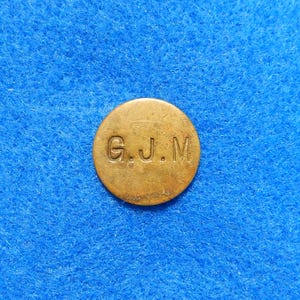 May include: A round, brass token with the letters "G.J.M" engraved on it.