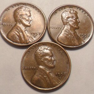 May include: Three copper-colored Lincoln pennies. Two pennies are dated 1957, and one is dated 1958. Each coin features a profile of Abraham Lincoln and the words "IN GOD WE TRUST" and "LIBERTY".