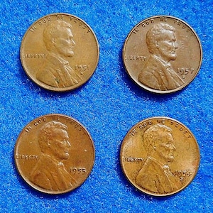 May include: Four copper-colored United States one-cent coins, each featuring the profile of Abraham Lincoln, the text IN GOD WE TRUST, LIBERTY, and the years 1951, 1957 D, 1955, and 1954 respectively, arranged in a two-by-two grid formation.