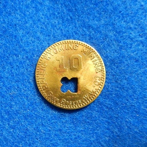 May include: A gold-colored metal token with the text "Paleic-Wyoming Mining Co. W.Va." and the number "10" in the center. The token has a small, cross-shaped hole in the center.