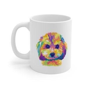 May include: A white ceramic mug featuring a colourful illustration of a poodle's face. The poodle's fur is a mix of yellow, orange, red, purple, blue, and green.