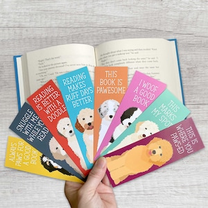 May include: A set of ten colorful bookmarks featuring different dog breeds and playful dog-themed sayings. The bookmarks are arranged in a fan shape, with the text facing outward. The sayings include "Reading is better with a doodle", "This book is pawsome", "I woof a good book", and "This marks my spot where you pawsed".