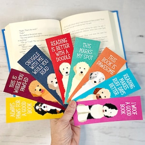 May include: Set of ten colorful bookmarks featuring doodle illustrations of dogs with various sayings. The sayings include "This is where you paws-ed", "Always paws for a good book", "Snuggle with me while you read", "Reading is better with a doodle", "This marks my spot", "This book is pawsome", "Reading makes ruff days better", "I woof a good book".