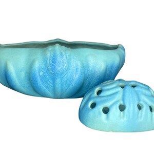 May include: A light blue ceramic bowl with a matching lid. The bowl has a scalloped rim and a textured, leaf-like design. The lid is domed with circular openings, also in light blue.