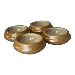 May include: Four small, handmade ceramic bowls. The bowls are a warm, earthy brown color with a slightly textured surface. Each bowl has a rounded shape with a small, shallow interior. The bowls are arranged together, suggesting a set.