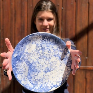 以下が含まれることがあります： 青と白の泡模様の白いセラミックプレート。プレートは人の手で持たれています。