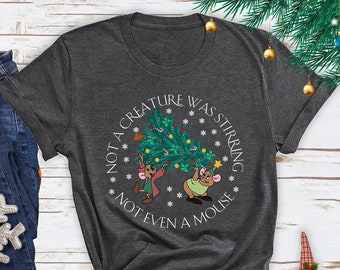May include: Dark grey heather t-shirt with a round graphic featuring a Christmas tree and two cartoon mice. The text reads "NOT A CREATURE WAS STIRRING, NOT EVEN A MOUSE." The shirt is paired with blue jeans, a red gift box, and a decorative snowflake.