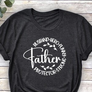 May include: A dark grey t-shirt with a white circle graphic that says "Husband, Hero, Funny, Strong, Protector, Father".